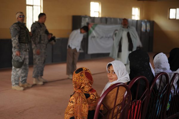 Glancing away from the Farah City Orphanage guests from the Farah Provincial Reconstruction Team, Fazana, an 11-year-old girl who completes her fourth grade studies at the orphanage and aspires to become a doctor, checks to see what other visitors in the room are up to behind her and her classmates, Dec. 10, Farah, Afghanistan. The 60 females are only at the orphanage during the day while the 78 boys stay overnight on bunk beds in an open barracks nearby. The orphanage, whose Afghan name translated in English, literally means "Kindergarteners," hosts children who do not have a father, brother, or other male figure in their lives who is responsible for their schooling and upbringing.